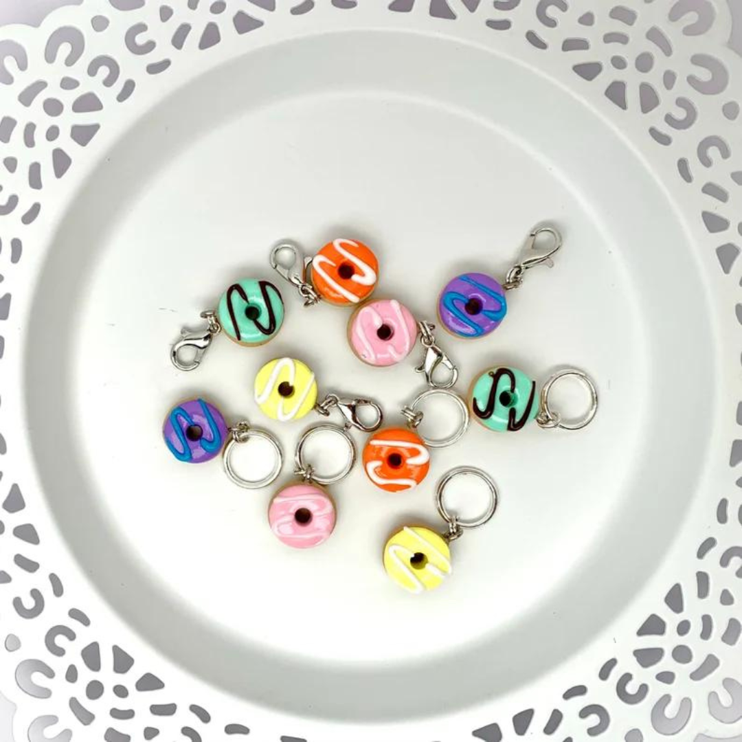 A handful of polymer clay donut stitch markers scattered on a plain white plate.