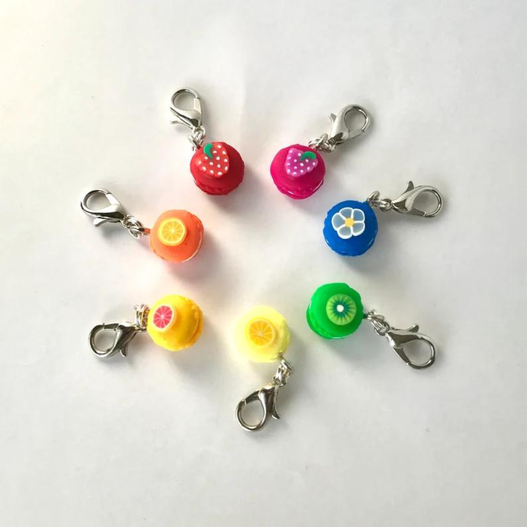 Seven polymer clay fruit macaron stitch markers arranged in a circle in the colors of the rainbow.