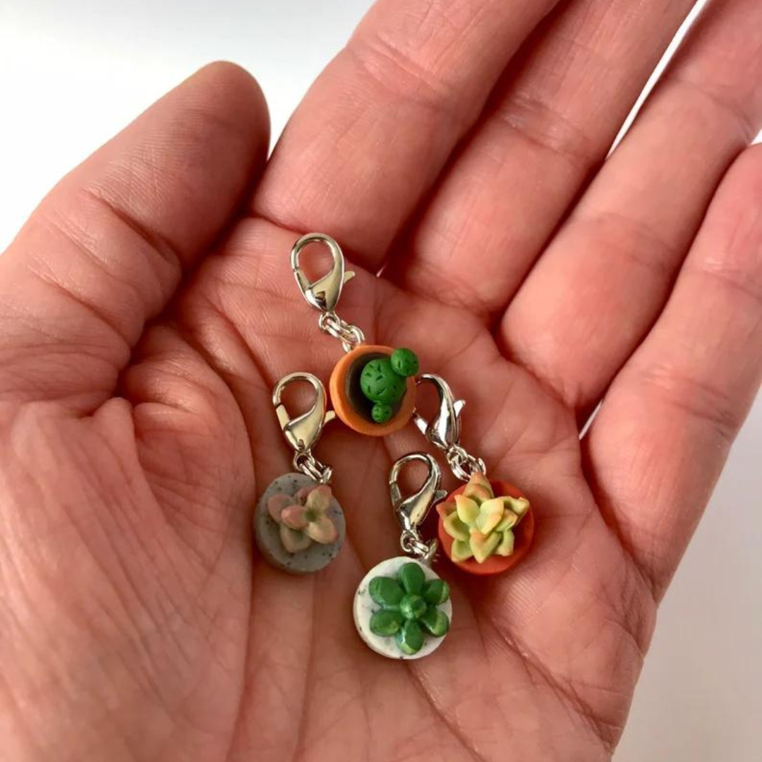 Four polymer clay charms held in the palm of a hand. Three are succulents in a pot, one is a cactus in a pot.