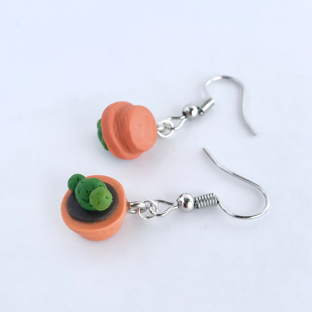Two polymer clay cactus in a pot earrings resting on a table.