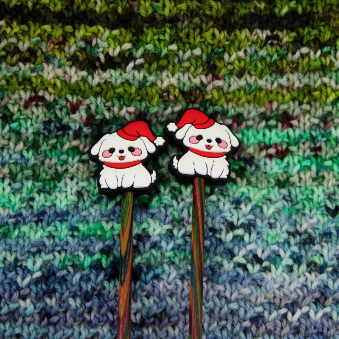 White dogs in red hats knitting needle stoppers on the ends of knitting needles.