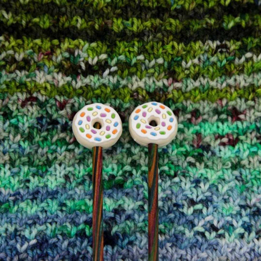 Donuts with rainbow sprinkles knitting needle stoppers on the ends of knitting needles.
