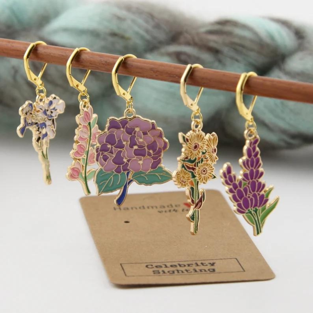 Five small flower stitchmarkers hanging on a wooden rod.