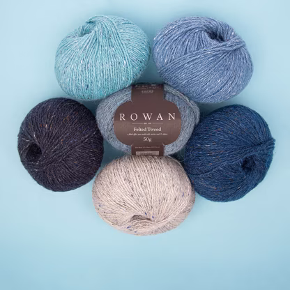 A set of six balls of blue Rowan Felted Tweed yarn arranged on a table.