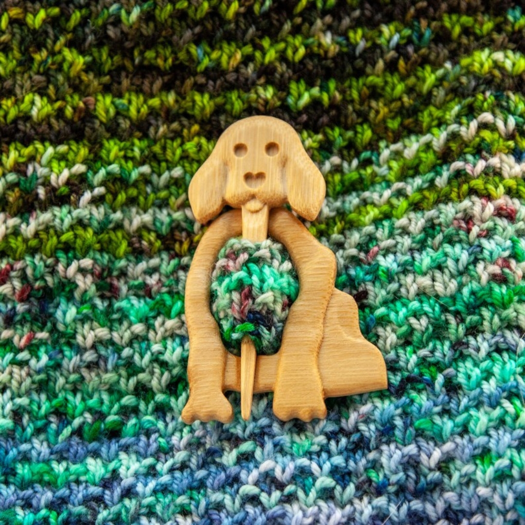 Wooden dog shawl pin on a variegated handknit fabric.