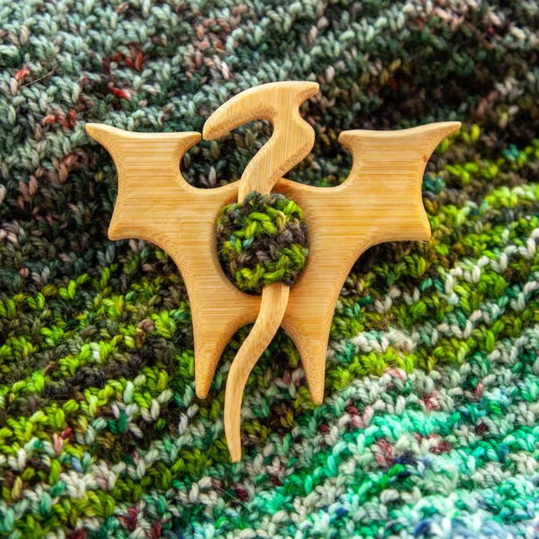 Wooden dragon shawl pin on a variegated handknit fabric.