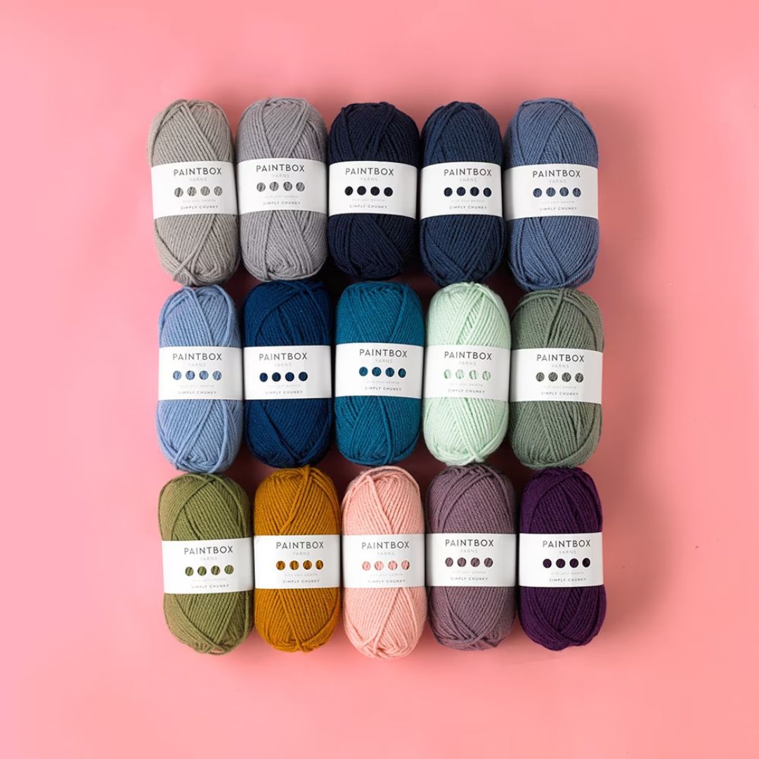 A pile of skeins of yarn in various colors laid flat on a table in a square.