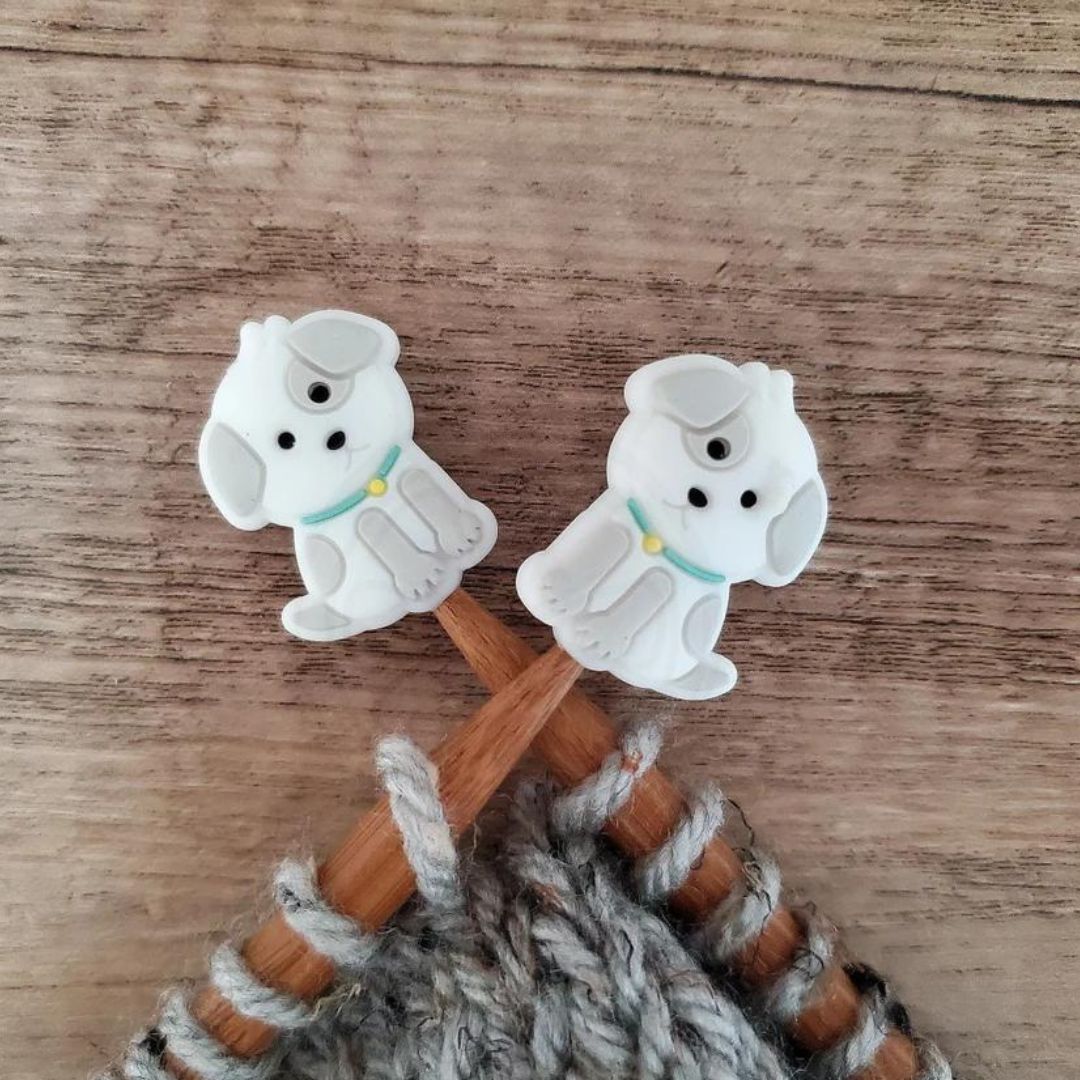 A pair of cute grey dog point protectors pictured on a pair of wooden knitting needles.