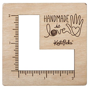 A square wooden tool with an L-shaped cut-out and ruler lines on the side, made to measure knitting swatches.