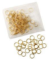 A set of golden loop stitch markers, some in a small plastic bag and some scattered around it.