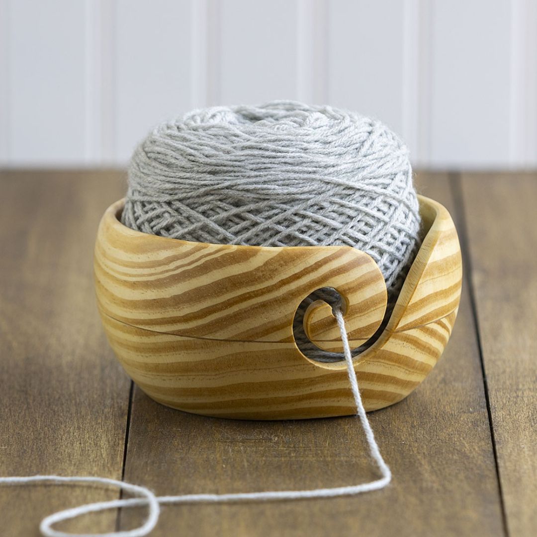 A light pine wooden yarn bowl with a striped appearance due to the wood grain.