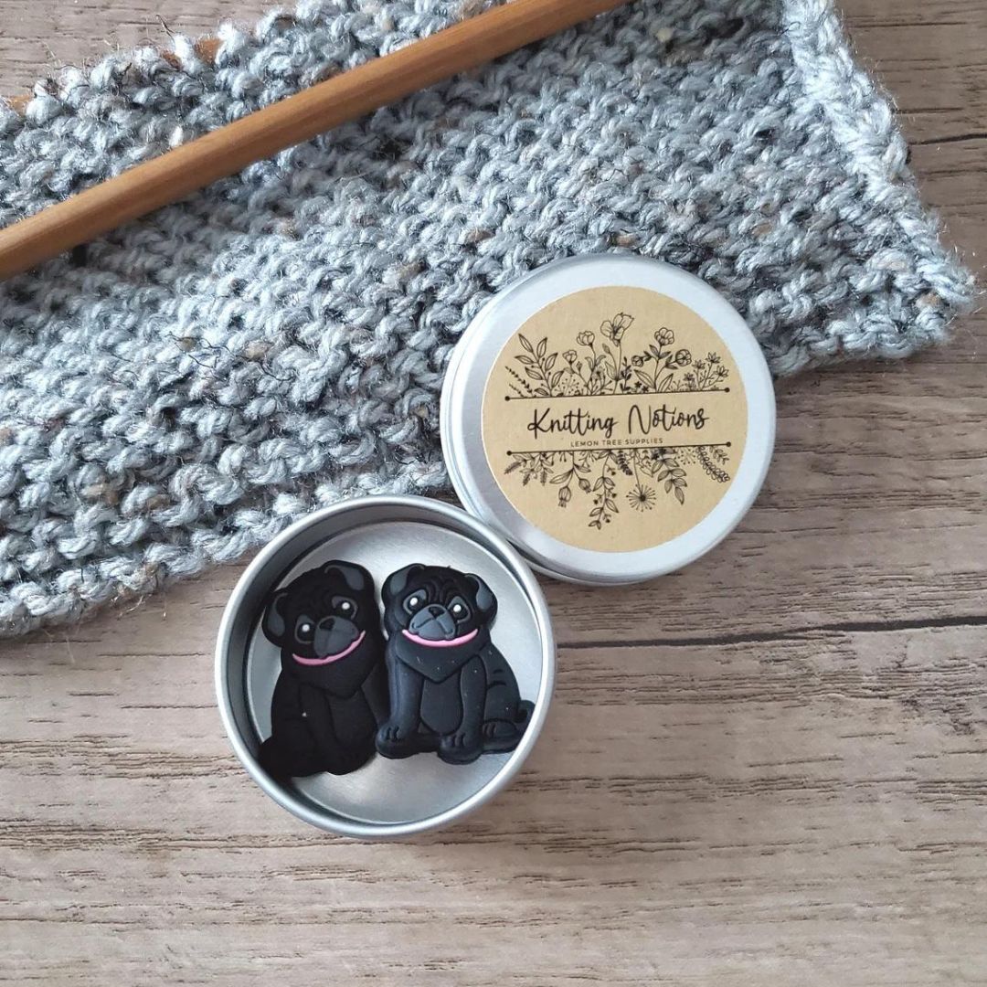 A set of black pug puppy stitch stoppers in a metal storage tin.
