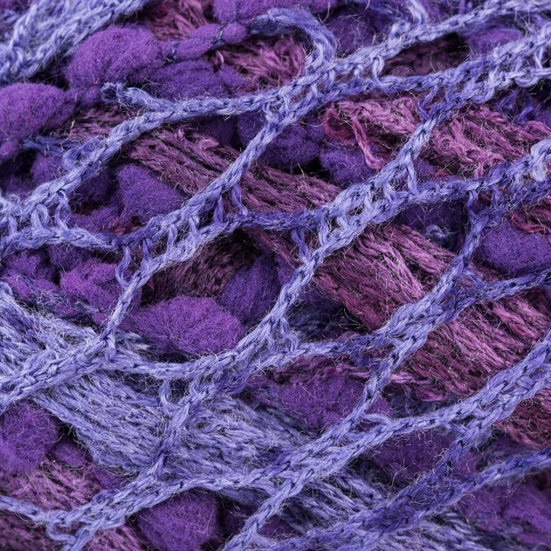 Close-up of purple and pink novelty yarn. It looks like a mesh when pulled apart and has pompoms along one edge.