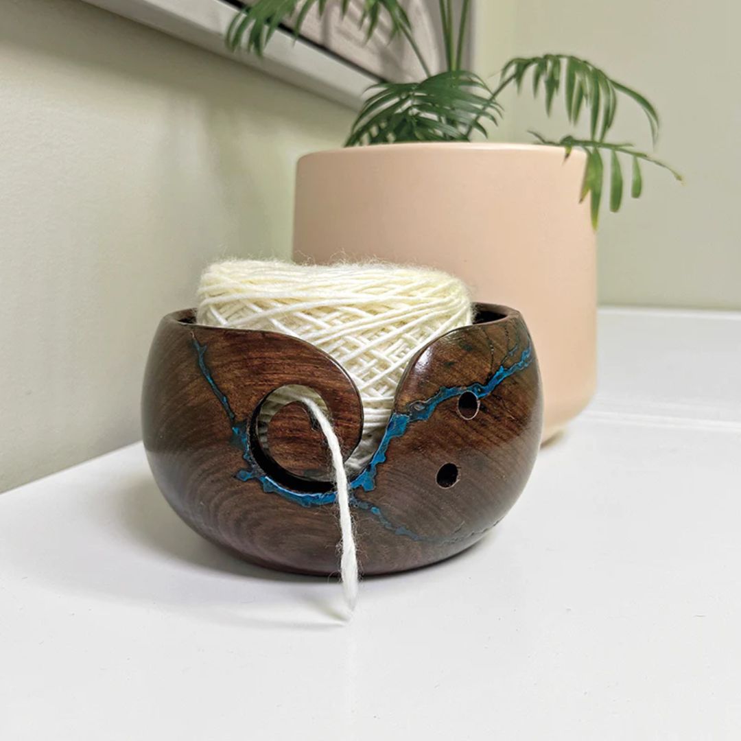 A dark, glossy wooden yarn bowl with a blue resin inlay around the opening.