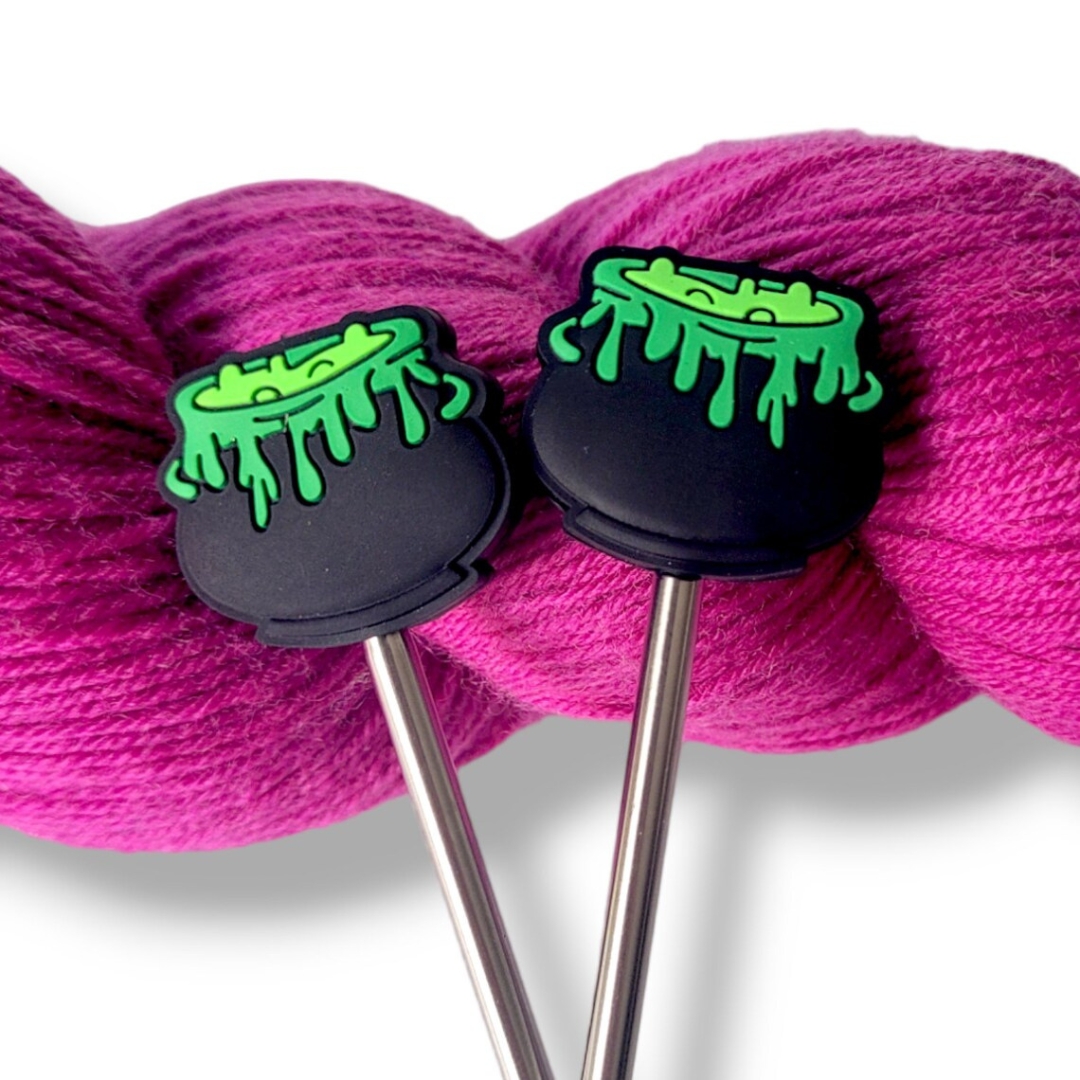 A set of knitting needle point protectors that look like cauldrons bubbling with a green potion.