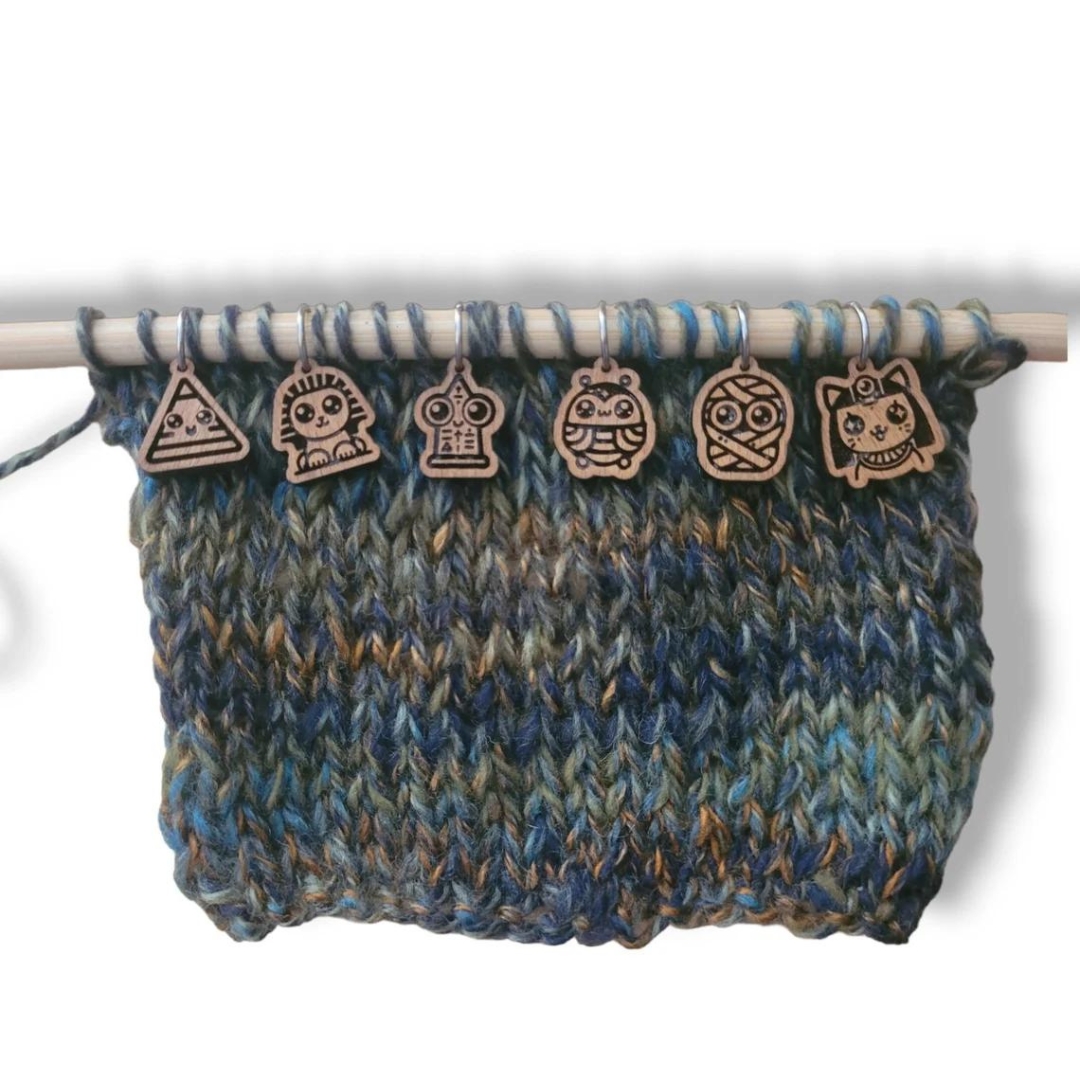 A set of six wooden Egypt-inspired knitting stitch markers displayed on a knitting needle.
