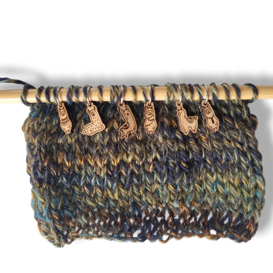 A set of six wooden llama knitting stitch markers displayed on a knitting needle.