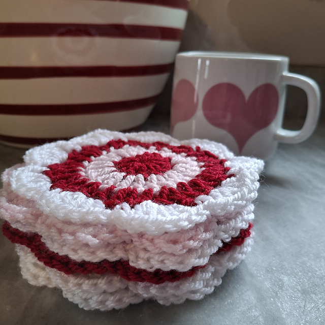 Stack of pink, red, and white crochet Helen's Coasters beside a heart mug