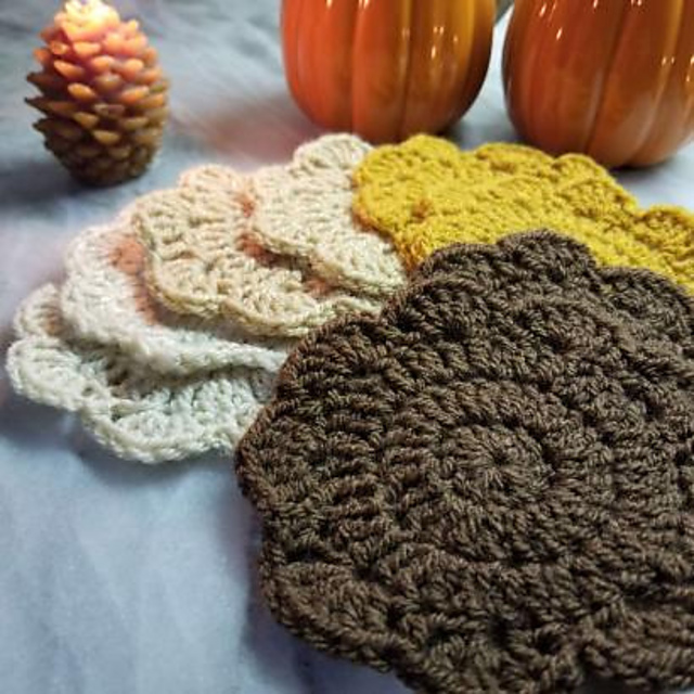 Stack of textured crochet Helen's Coasters in neutral, yellow, and brown yarn beside pumpkins